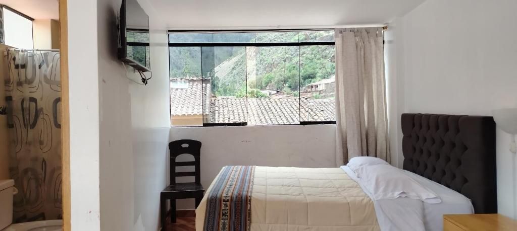 A bedroom with a bed, a chair, a window with a view of a village, and a television on the wall.