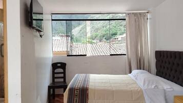 Une chambre à coucher avec un lit, une chaise, une fenêtre donnant sur un village et un téléviseur fixé au mur.