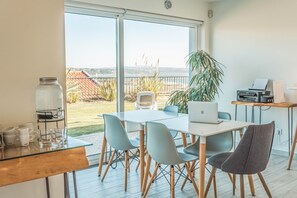 Espaço de escritório moderno com uma grande janela com vista para um jardim e para o mar.