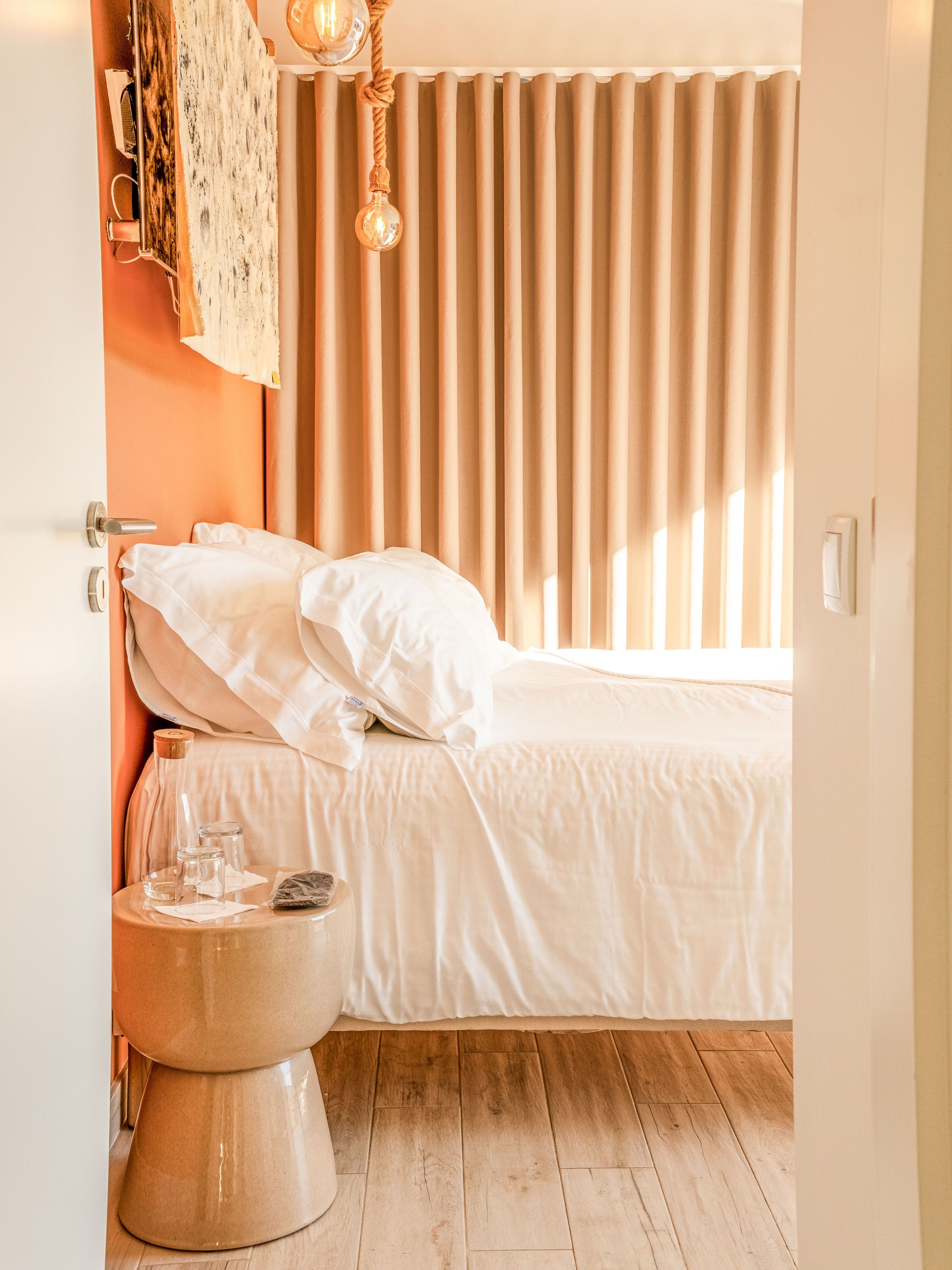 A bedroom with a bed, a bedside table, a radiator, and a window with curtains.