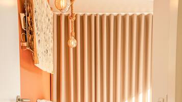 A bedroom with a bed, a bedside table, a radiator, and a window with curtains.