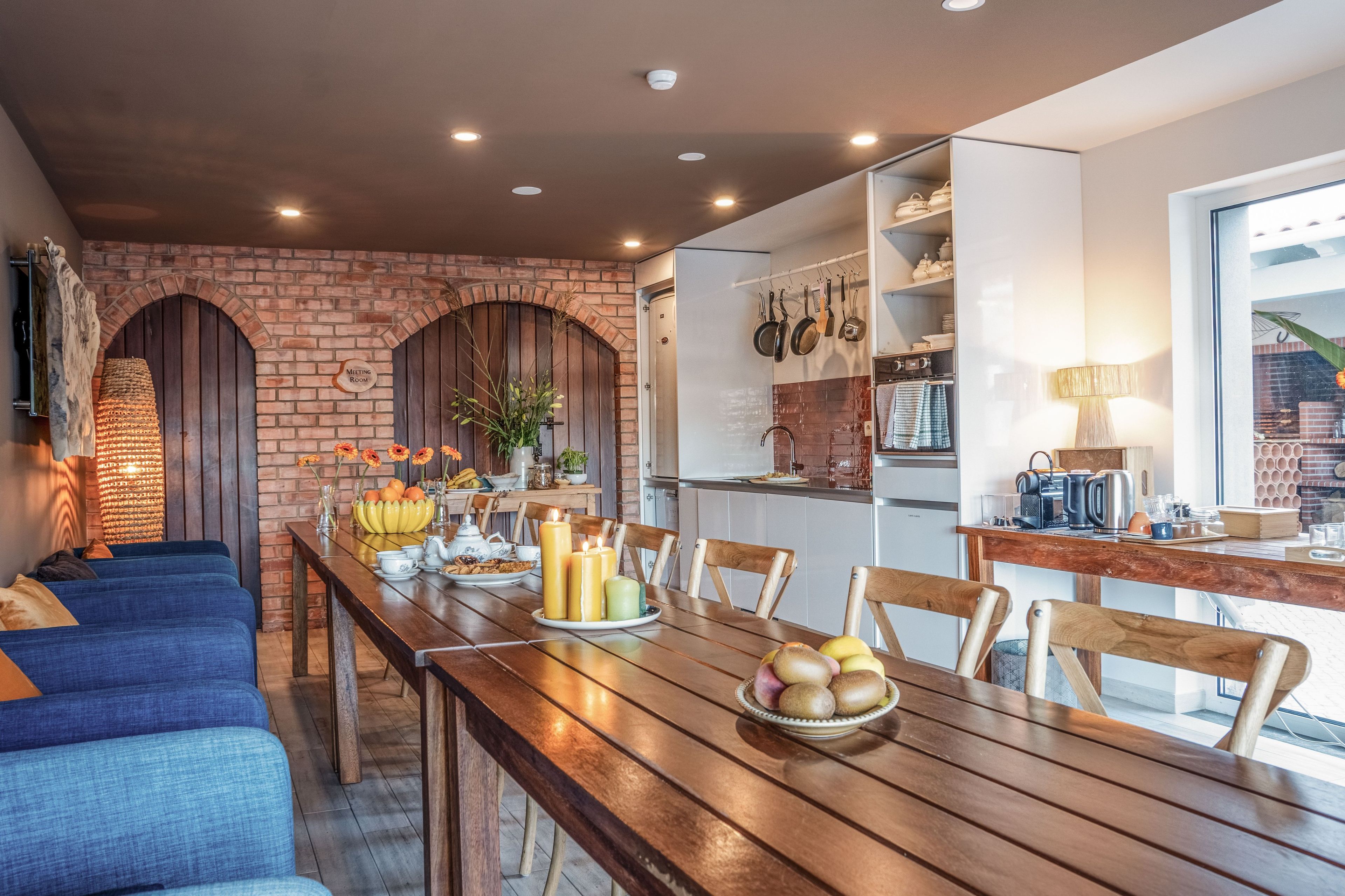 A dining area with a long wooden table, chairs, and a kitchen in the background.