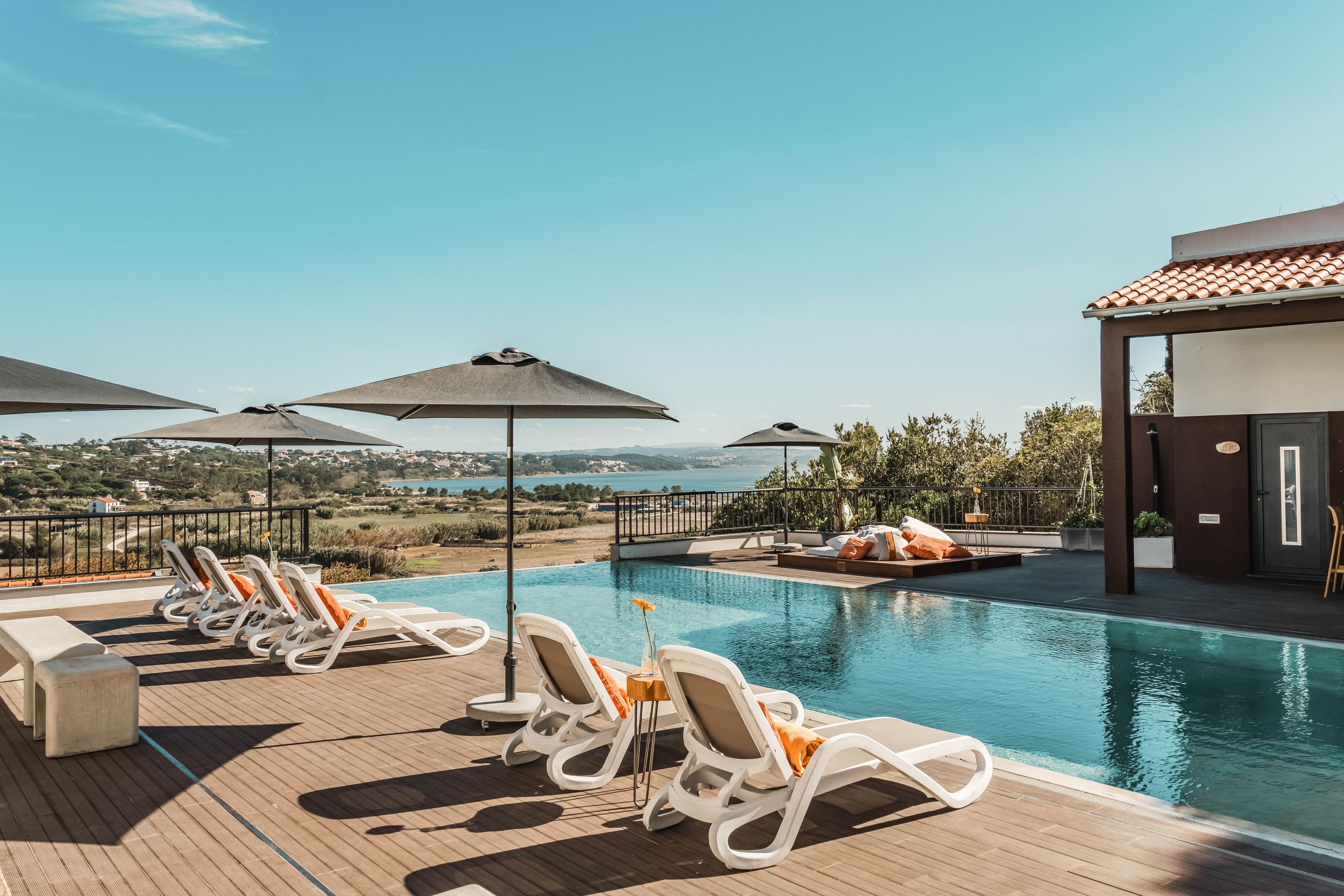A poolside area with lounge chairs and umbrellas, overlooking a scenic view.