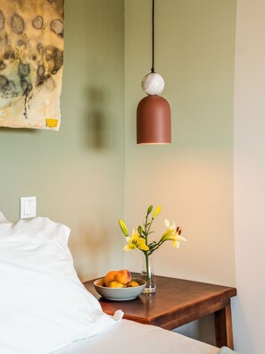 Quarto de hotel com cama, mesa de cabeceira com um vaso de flores e luminária na parede.