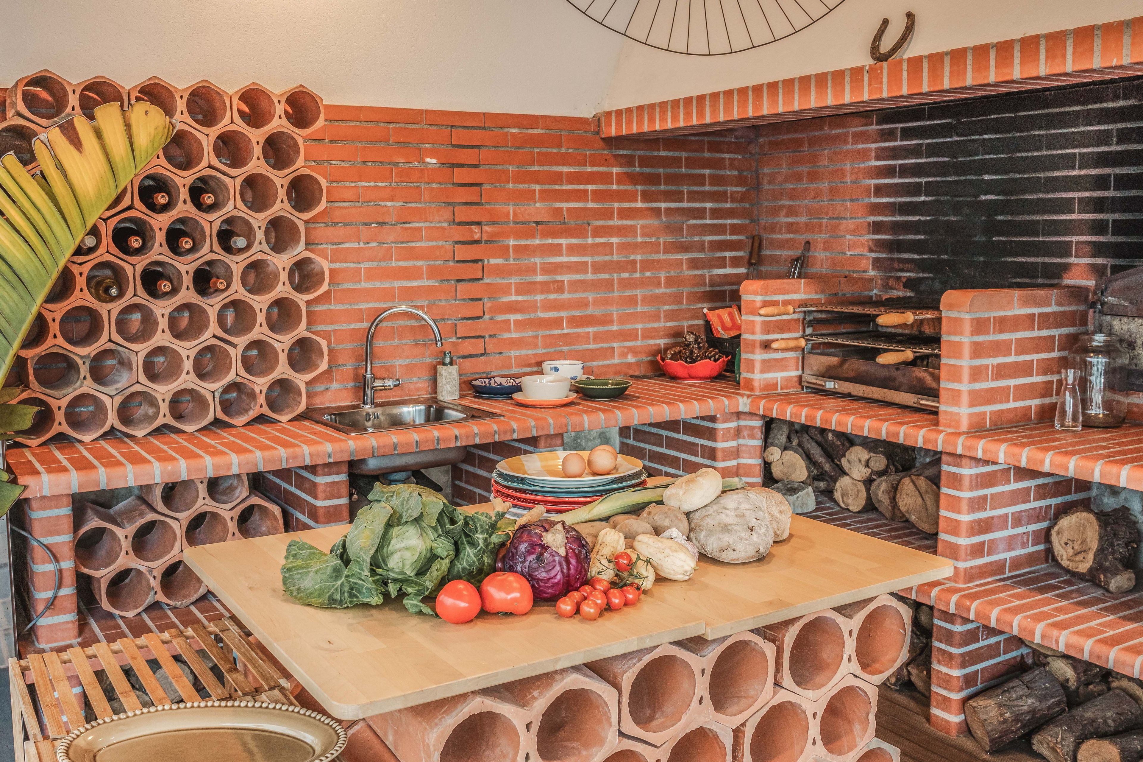 Uma cozinha com parede de tijolos, pia e mesa de madeira com legumes.