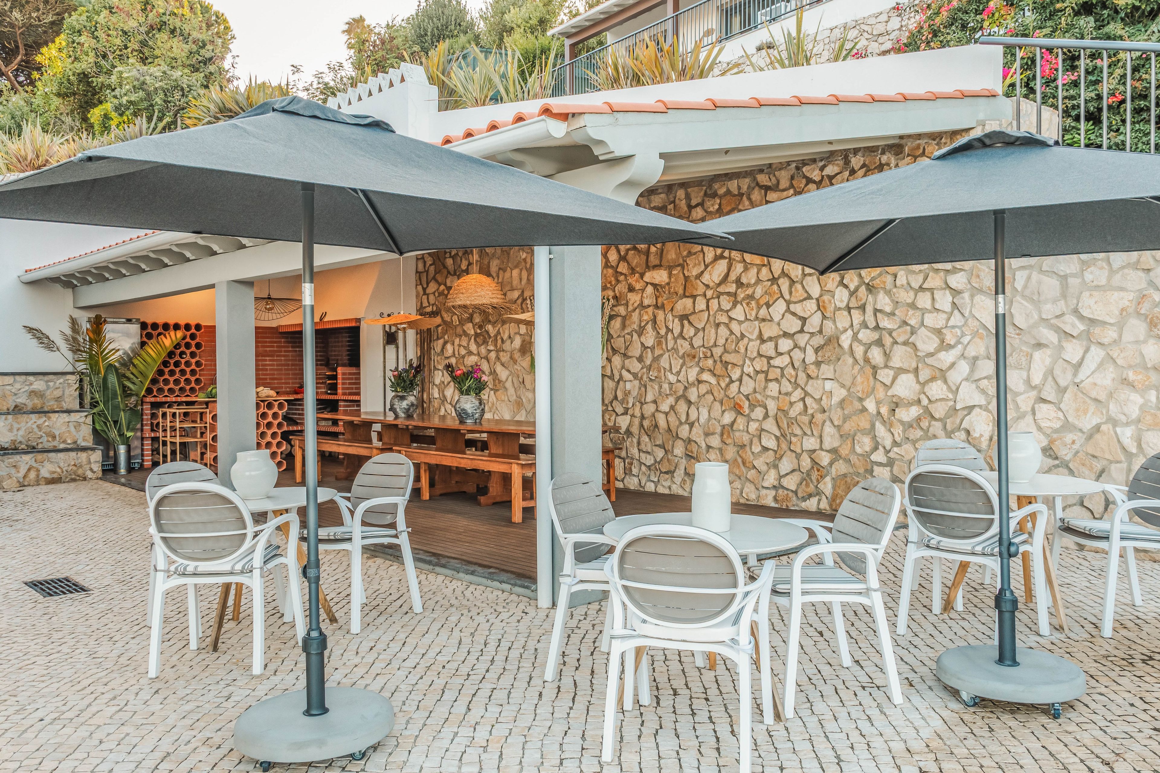 An outdoor patio with white chairs and tables, stone walls, and umbrellas.