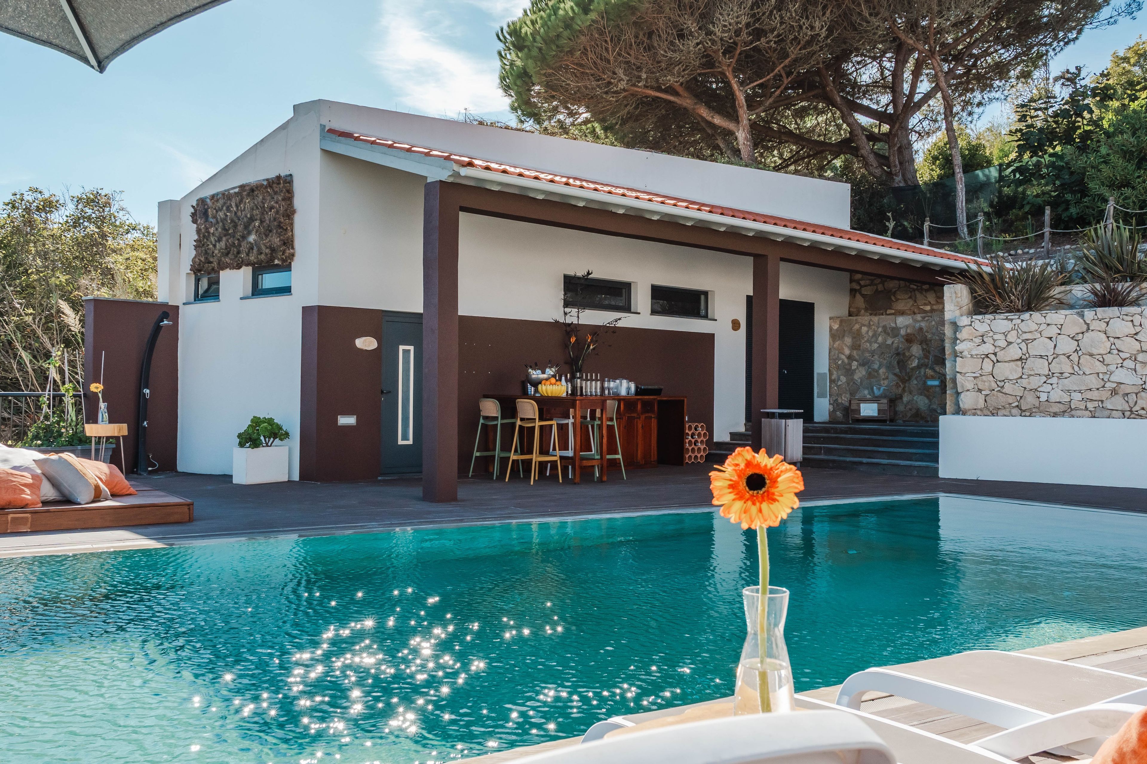 A modern house with a swimming pool, outdoor seating, and a stone wall.