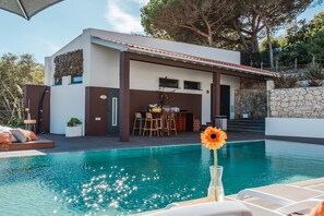 Une maison moderne dotée d’une piscine, d’un espace salon extérieur et d’un mur en pierre.