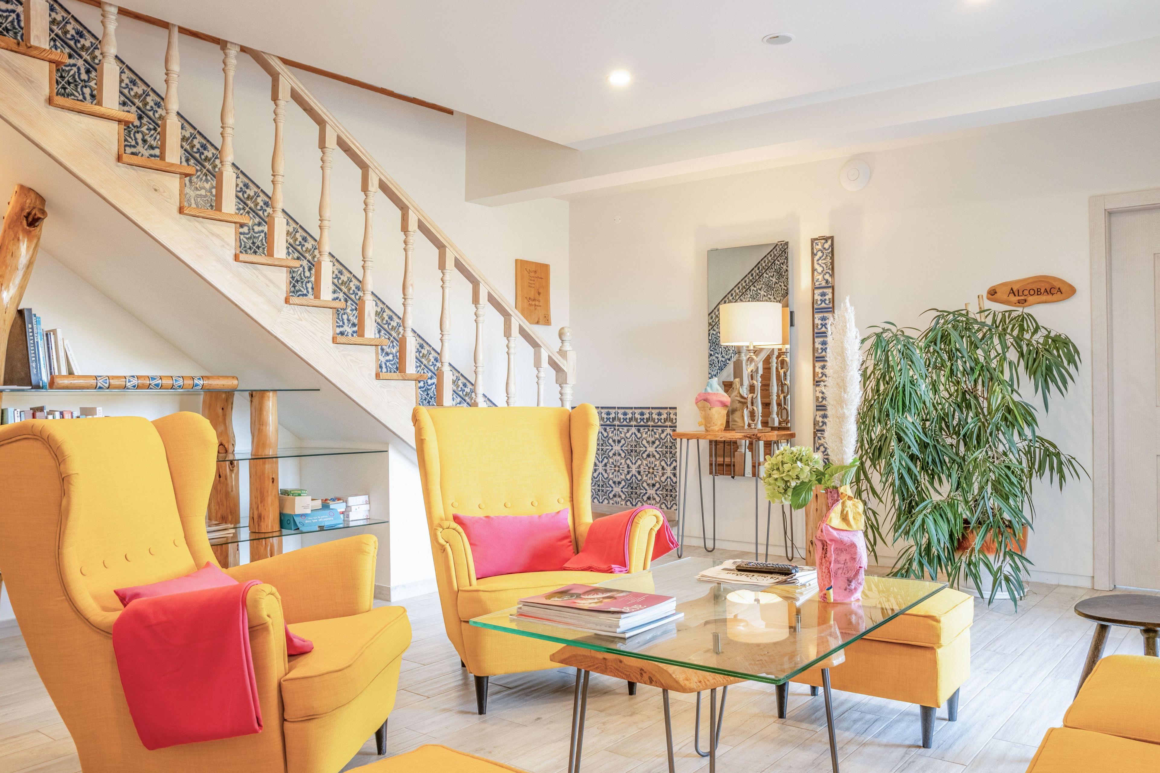 Un vaste espace de vie comprenant un escalier, des fauteuils jaunes, une table basse en verre et une grande plante en pot.