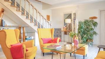 Un vaste espace de vie comprenant un escalier, des fauteuils jaunes, une table basse en verre et une grande plante en pot.