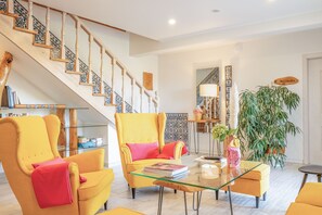 Un vaste espace de vie comprenant un escalier, des fauteuils jaunes, une table basse en verre et une grande plante en pot.