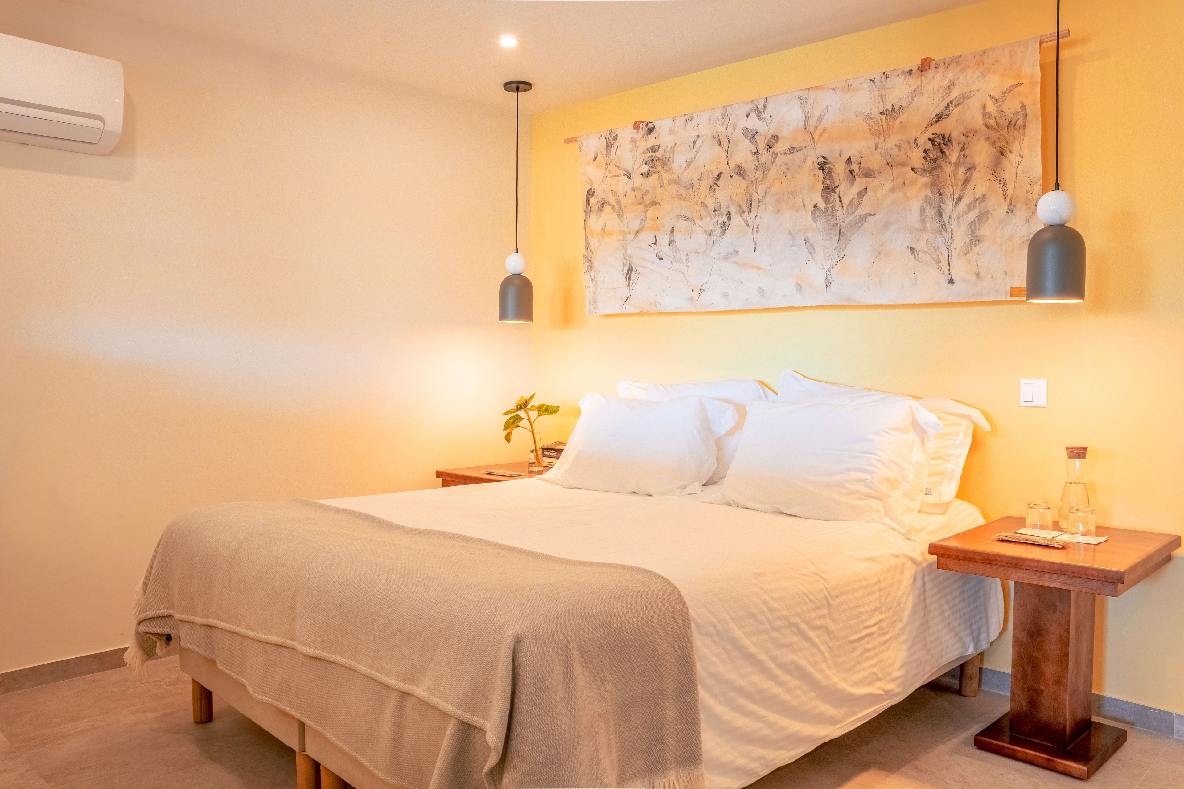 Una habitación de hotel con cama, mesita de noche, aire acondicionado de pared y un cuadro.