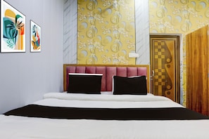 A bedroom with a bed, two pillows, a headboard, a wall with a floral pattern, and a door with a geometric design. - Super Hotel O Banaras Junction BLW (Varanasi)