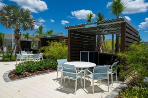 Un espace extérieur aménagé en terrasse, avec des chaises blanches et une table ronde, entouré de palmiers et agrémenté d’une pergola.