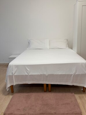 A bed with white bedding, a wooden headboard, and a pink rug on a wooden floor. - New Listing (Venezia)