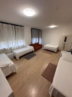 A room with two single beds, a sofa, a wardrobe, and a window with curtains. - New Listing (Venezia)