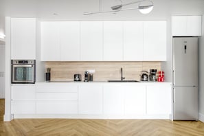 Een moderne keuken met witte kastjes, een houten spatwand en roestvrijstalen apparatuur.