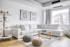Een moderne woonkamer met een witte bank, een glazen salontafel en twee abstracte kunstwerken aan de muur.