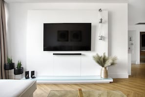 Een moderne woonkamer met een flatscreen televisie aan een witte muur, een glazen salontafel en een minimalistische inrichting.