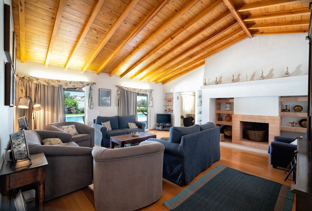 A spacious living room with a high wooden ceiling, a fireplace, and a television.