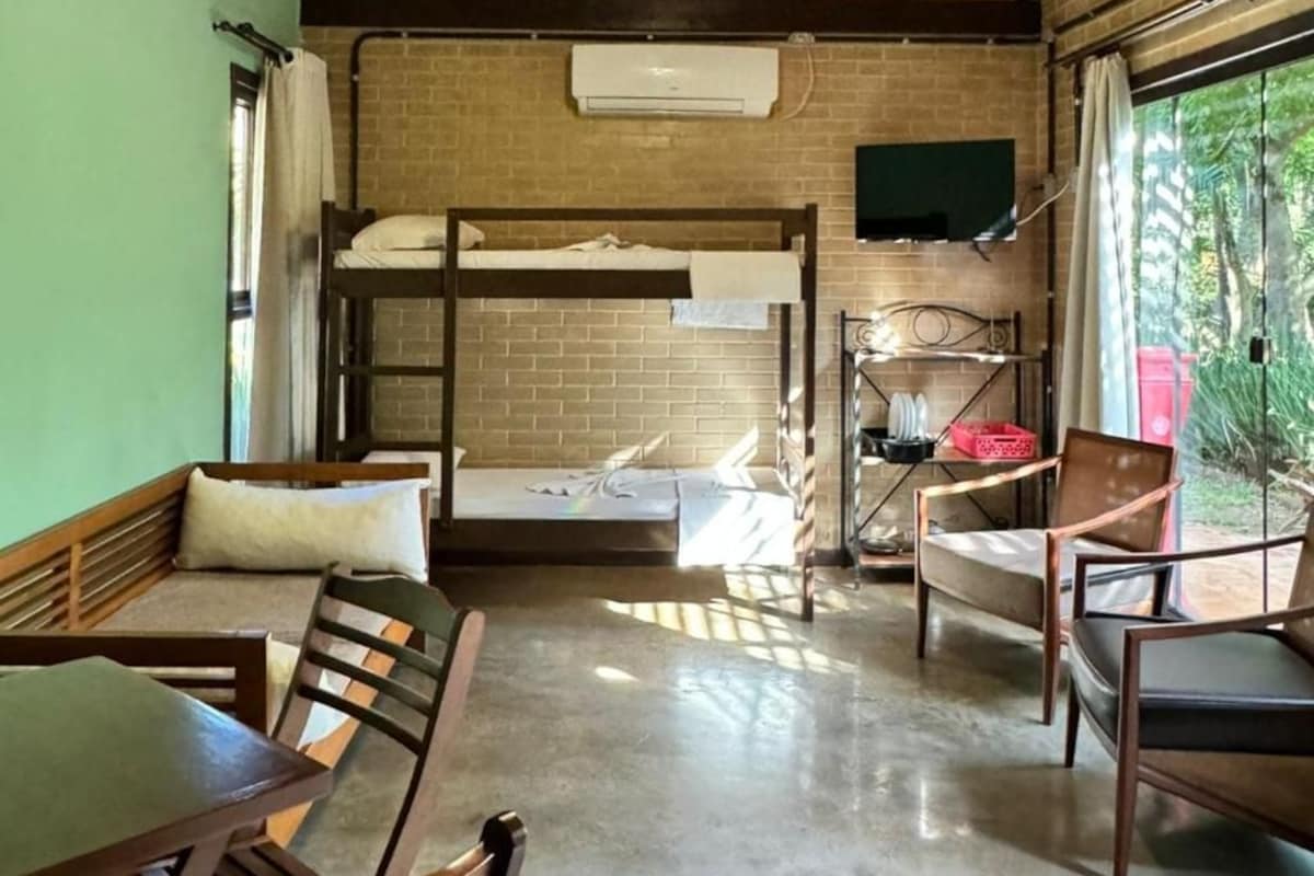A bunk bed with a flat-screen TV above it, a dining table with chairs, and a window with curtains.