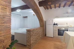 A compact room with a bed, a small kitchenette, and a brick partition.