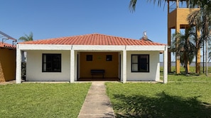 Un edificio de dos pisos con techo de tejas rojas, un pequeño porche y una banca.