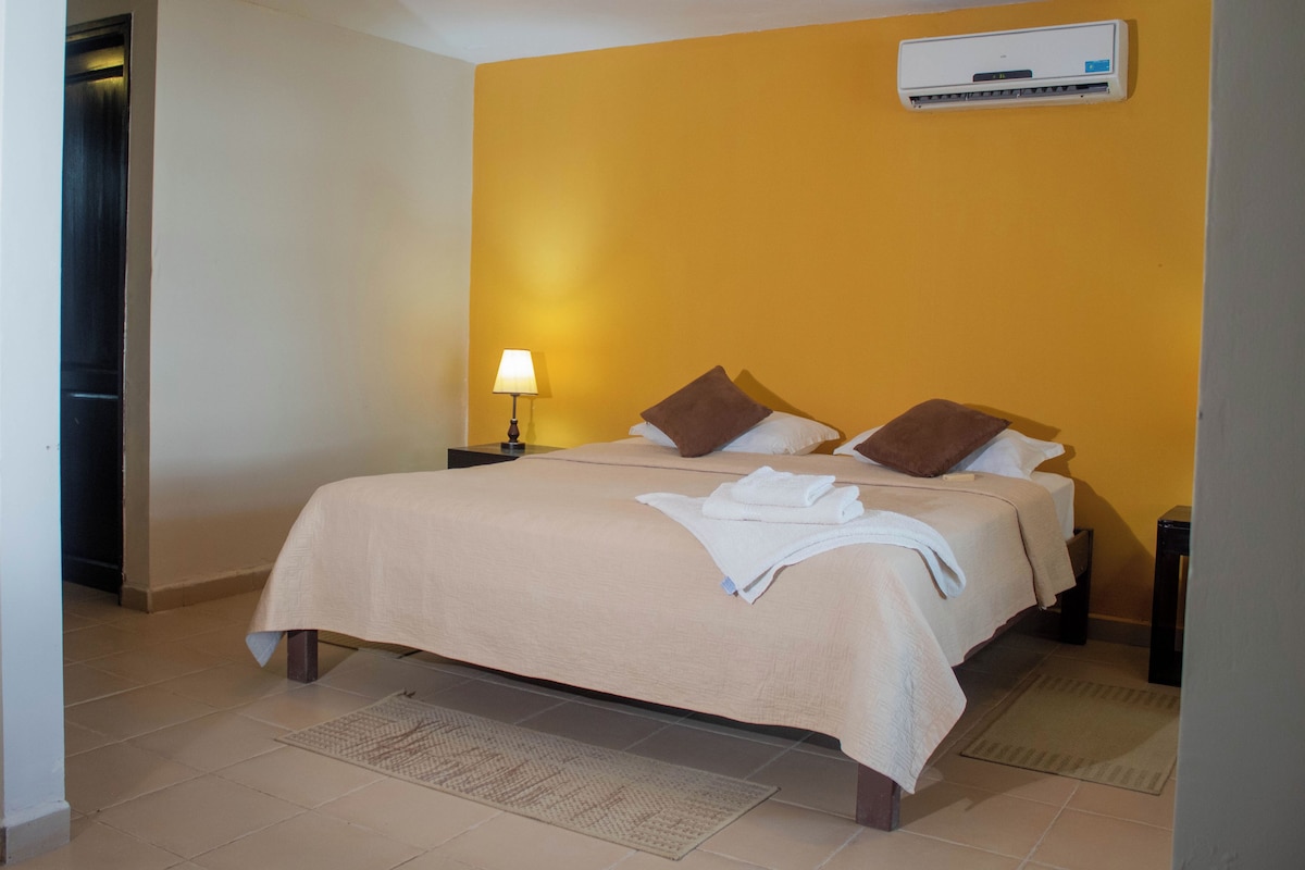 Una habitación de hotel con cama, mesita de noche, lámpara y unidad de aire acondicionado en la pared.