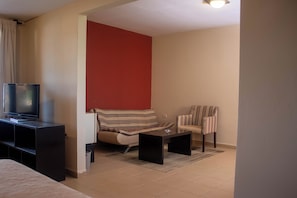 Un espacio habitable compacto con una televisión sobre un mueble bajo, un sofá, un sillón a rayas y una pequeña mesa de centro.
