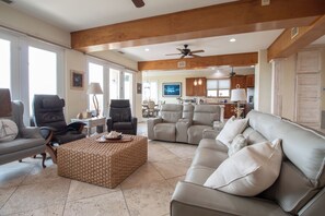 A spacious living room with a grey sofa, a woven ottoman, and a dining area in the background. - Here Awhile-30 Day Oceanfront Escape (Folly Beach)