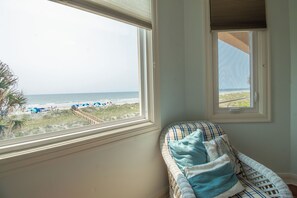 A room with a view of the beach, a wicker chair with cushions, and a window with blinds. - Here Awhile-30 Day Oceanfront Escape (Folly Beach)