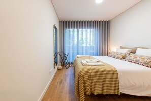 Ein Hotelzimmer mit einem großen Bett, einem Vorhangfenster, Holzboden und Blick auf Grünflächen.