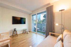 Ein modernes Wohnzimmer mit einem Flachbildfernseher, einem Glastisch, einer Couch und einer großen Schiebeglasdoor, die zu einem Außenbereich führt.