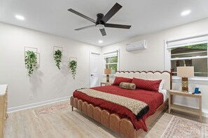 Een slaapkamer met een bed, een plafondventilator, een airconditioning en een raam met uitzicht op groen.