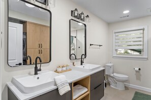 Een moderne badkamer met twee wasbakken, een toilet en een raam met zonwering.