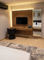 A hotel room with a bed, a desk with a flat-screen TV, a chair, and a mirror.