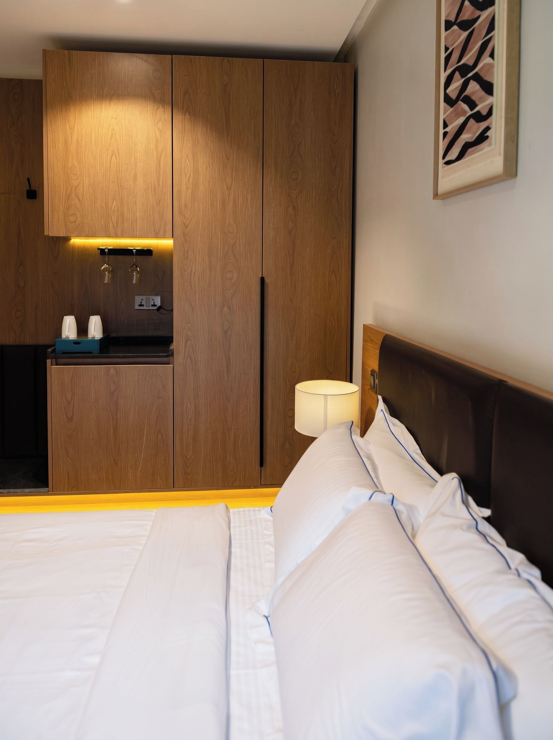 A hotel room with a bed, a bedside table, a nightstand, a wall-mounted lamp, and a built-in wardrobe.