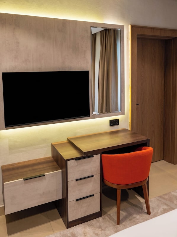 A modern desk with a flat-screen TV, a window with curtains, and a chair.