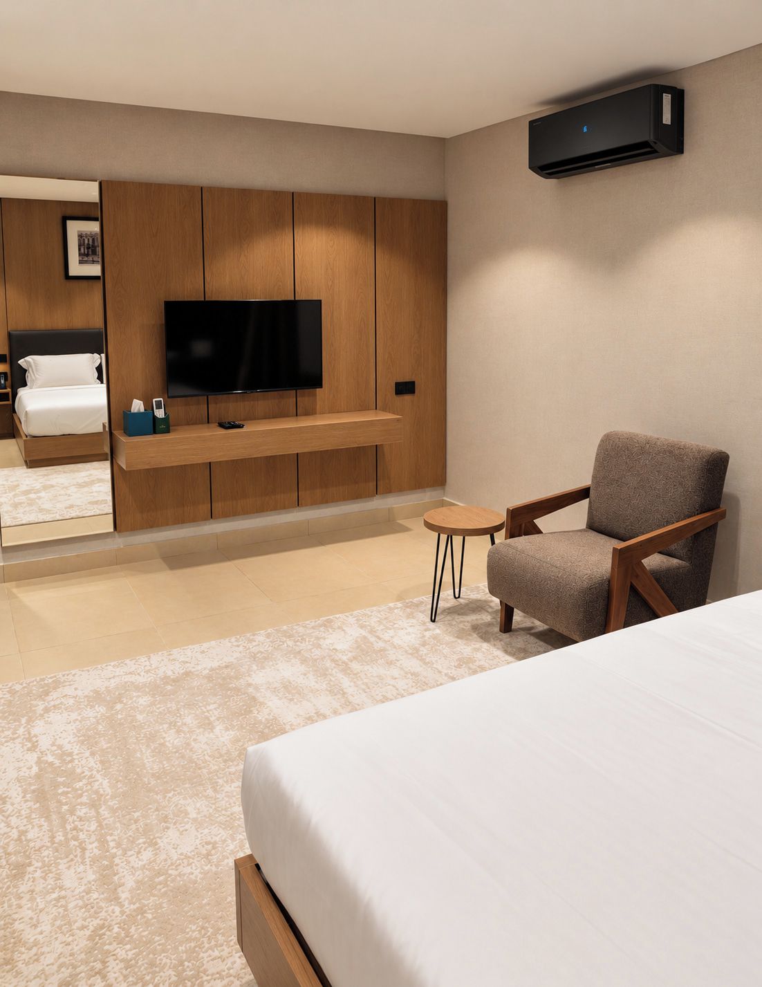 A modern hotel room with a bed, a television, a seating area, and an air conditioning unit.