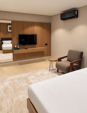 A modern hotel room with a bed, a television, a seating area, and an air conditioning unit.
