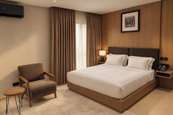 A hotel room with a large bed, a chair, a bedside table, a lamp, and a framed picture on the wall.