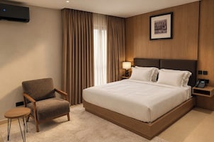 Habitación de hotel con una cama grande, una silla, una mesita de noche, una lámpara y un cuadro en la pared.