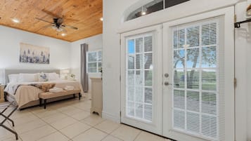 Un dormitorio con cama, ventilador de techo, un cuadro y ventana con persianas.