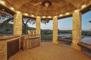 Une terrasse extérieure dotée d’une structure en colonnes de pierre, d’un barbecue intégré et offrant une vue sur le paysage environnant.