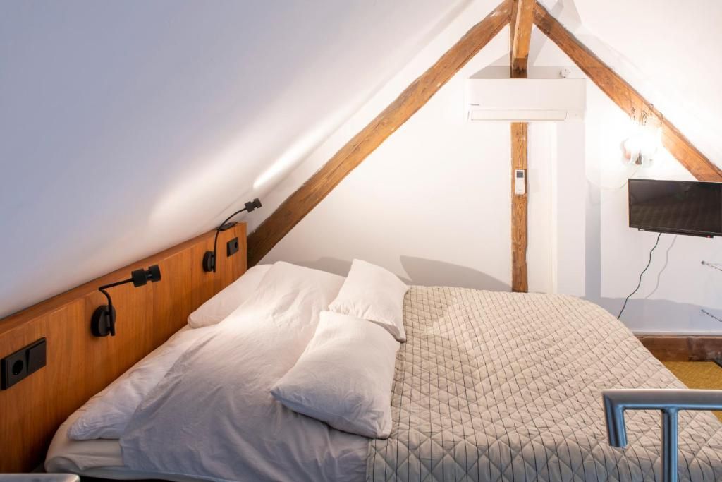 Une chambre avec un plafond en pente, un lit avec une literie blanche, un téléviseur fixé au mur et une tête de lit en bois.