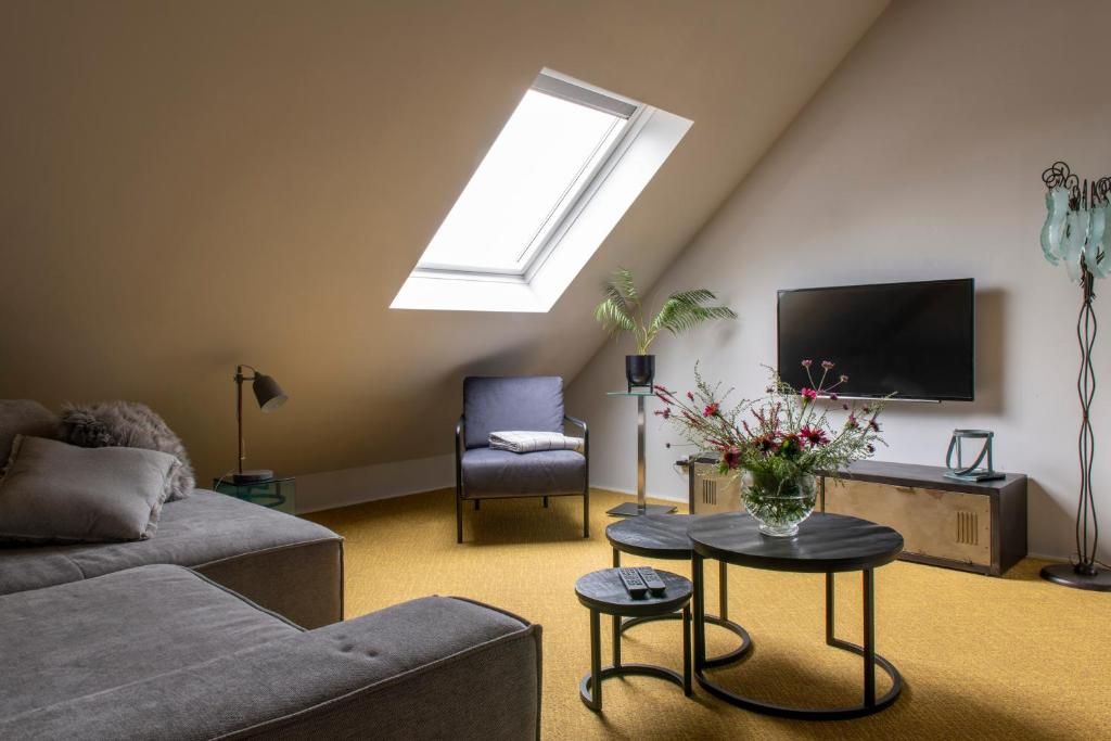 Un salon moderne doté d’une lucarne, d’un téléviseur à écran plat, d’un canapé, d’un fauteuil et d’une petite table sur laquelle est posé un vase de fleurs.