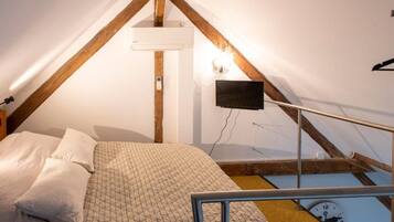 A bedroom with a bed, a wall-mounted TV, a clock, and a wooden ceiling beam structure.