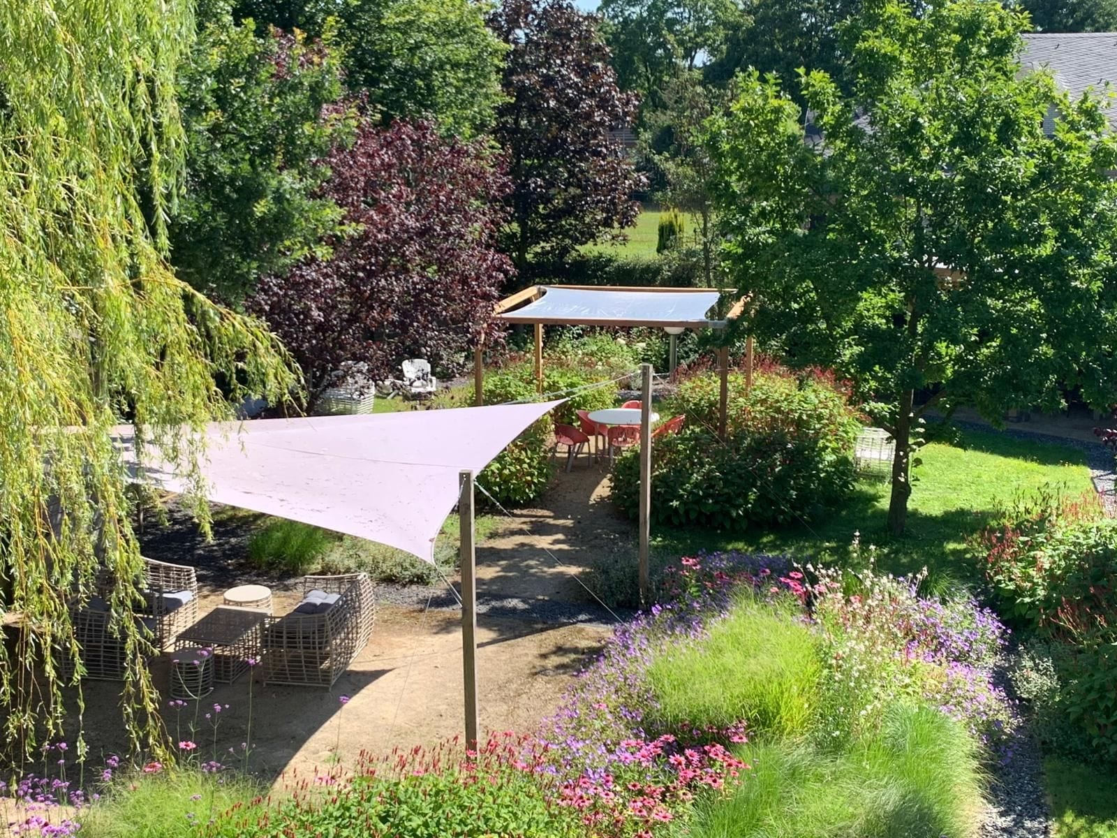 Un jardín con un pérgola, una zona de estar y diversas plantas.