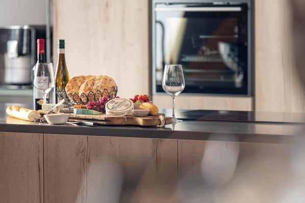 A wooden counter with a variety of food items, including bread, cheese, and grapes, and two wine glasses.