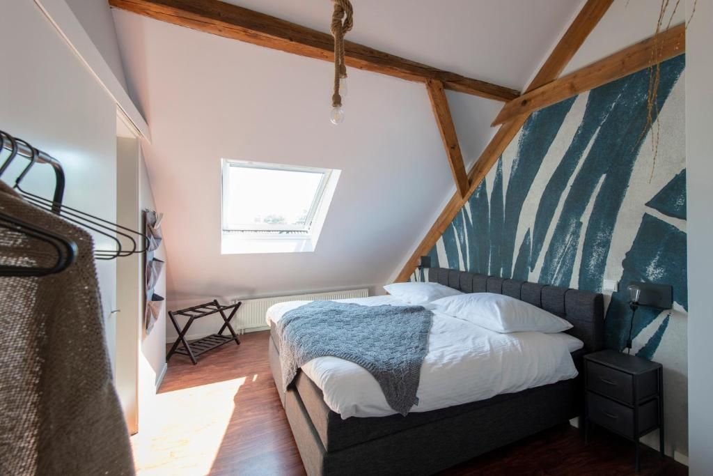 Un dormitorio con techo inclinado, una cama con ropa de cama blanca, una mesita de noche pequeña y una ventana con luz natural.